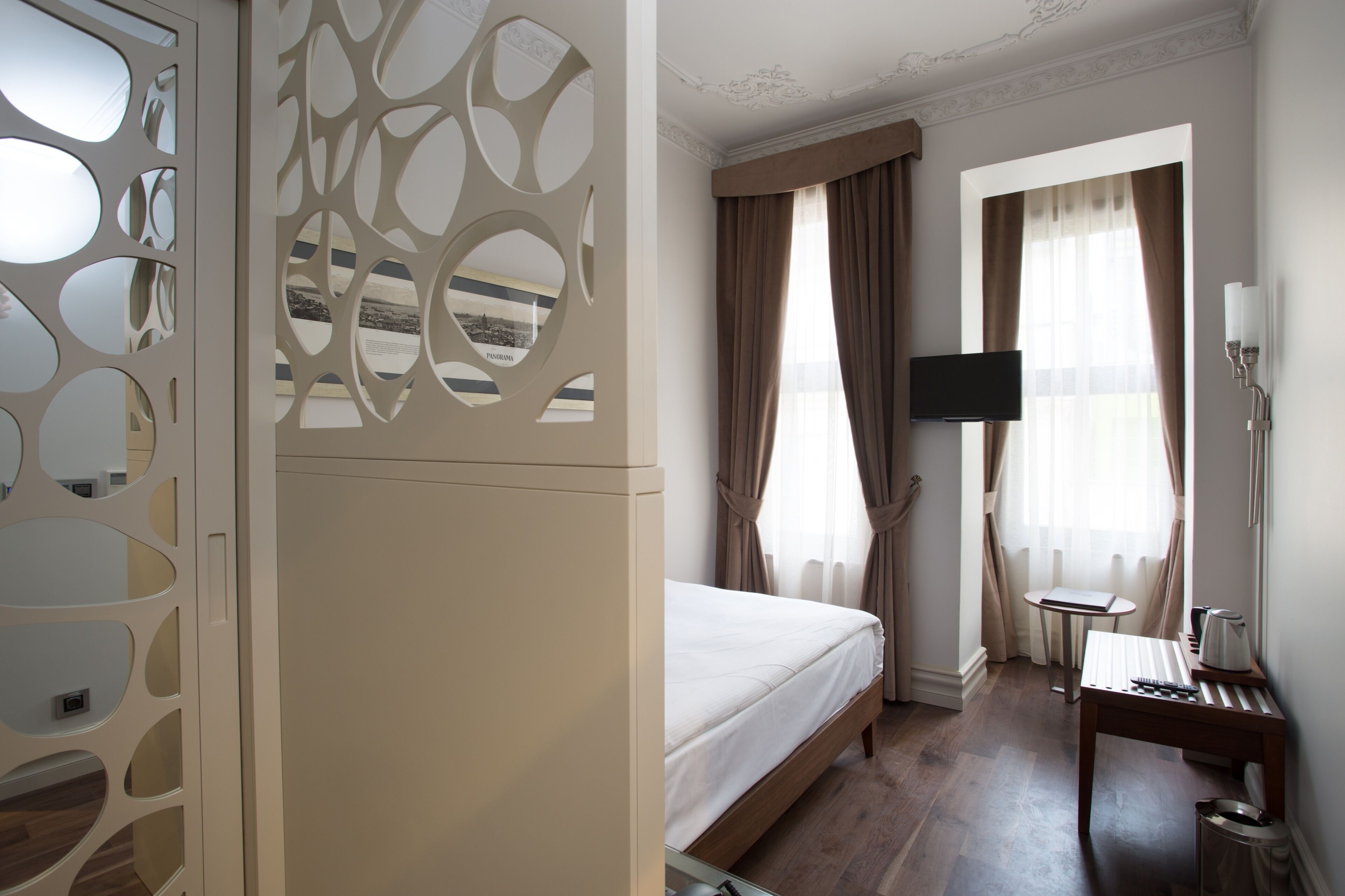 Una habitación de hotel con cama, escritorio con lámpara, televisor y ventana con cortinas.