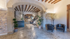 Un vestíbulo amplio con piso de mármol, pared de piedra y techo de madera. Hay dos sillones de cuero y una planta en maceta.
