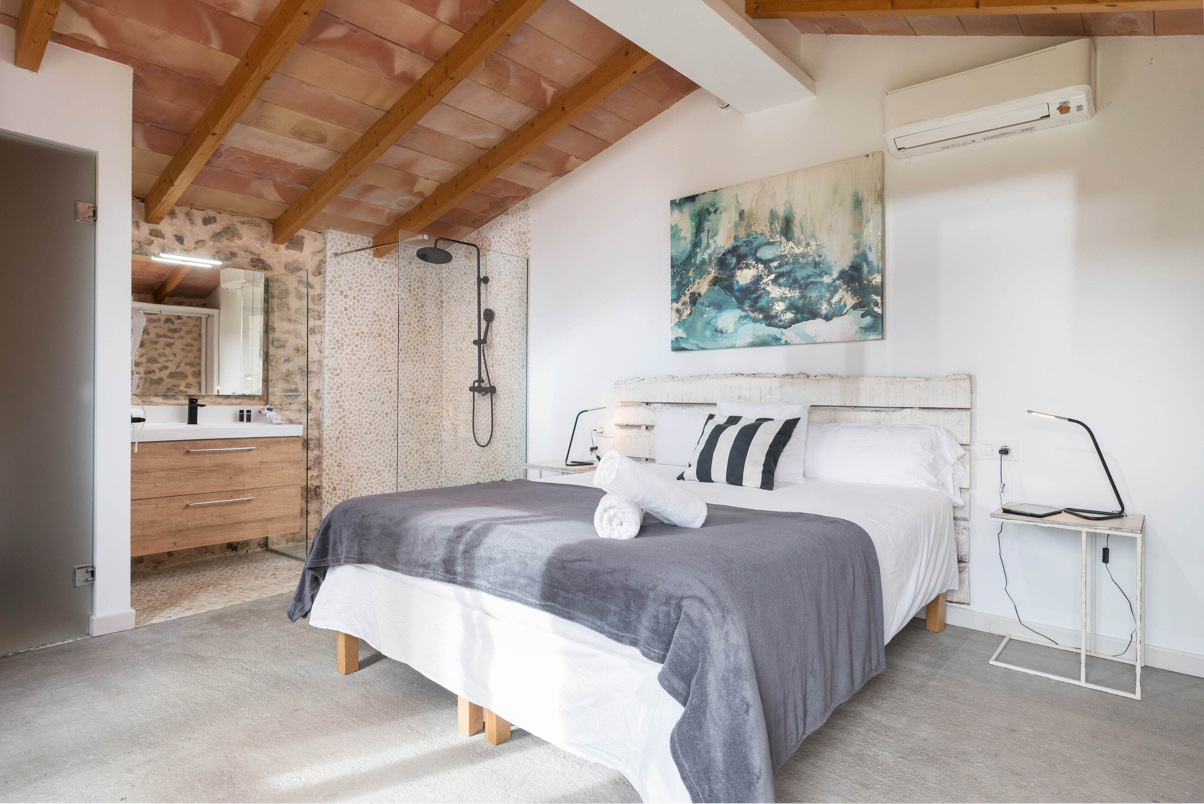 Un dormitorio con cama, mesita de noche, espejo, ducha y un cuadro en la pared.