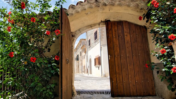 Una puerta de madera abierta que da a una calle adoquinada flanqueada por edificios.