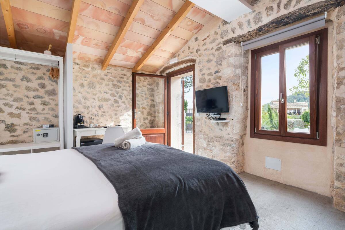 Ein Schlafzimmer mit Bett, Schreibtisch mit Computer, Fernseher und Steinwand.