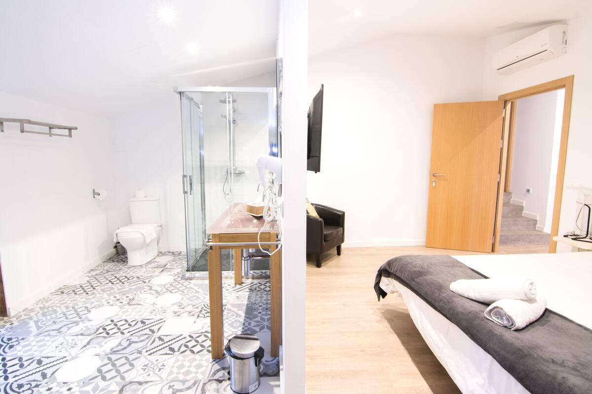 Ein modernes Badezimmer mit einem gemusterten Boden, einer Glasdusche und einem Holztisch. Das Zimmer verfügt über eine weiße Toilette und ein Waschbecken mit Handtuchhalter.
