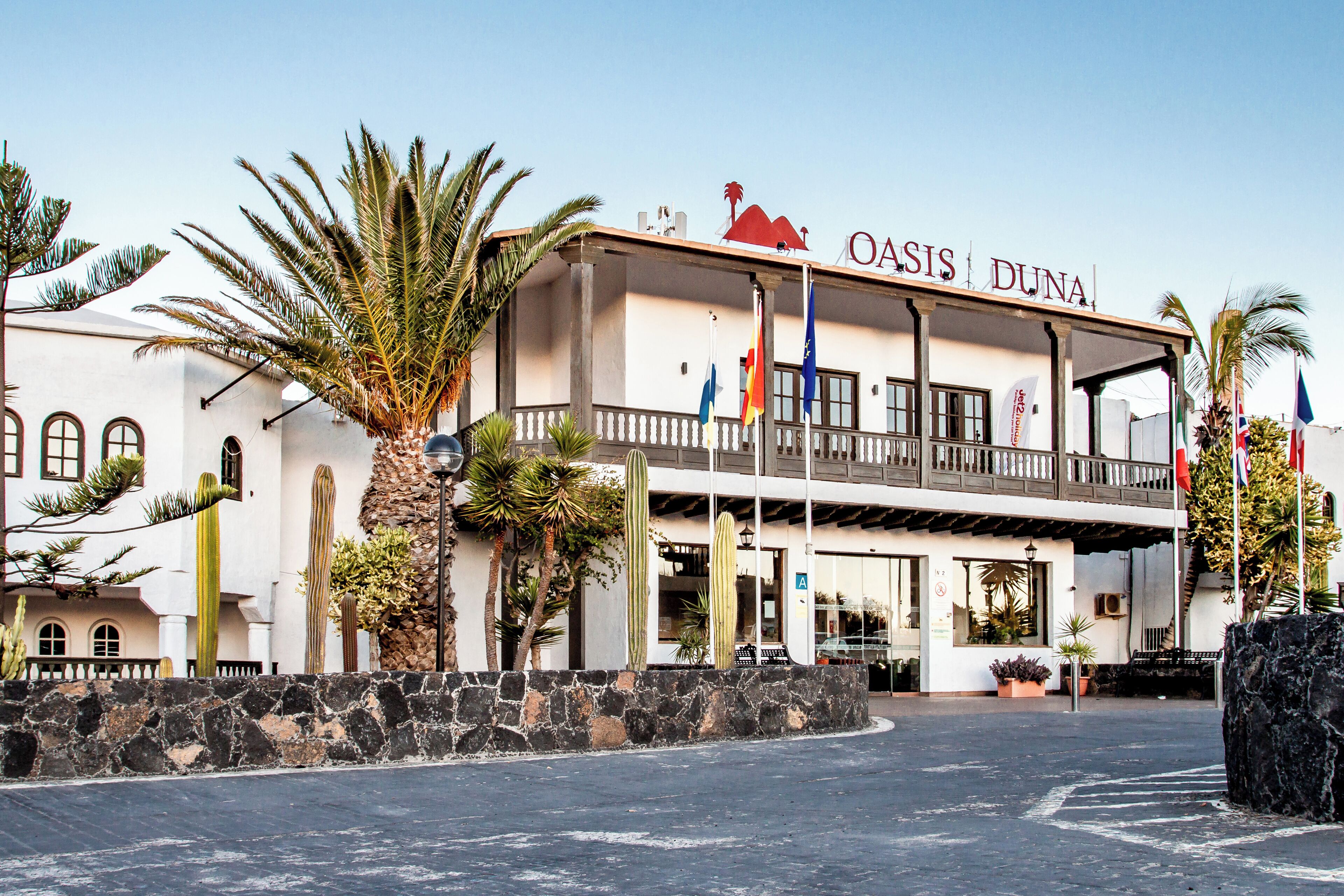 A building with a sign reading 'Oasis Dunas' and multiple flags.