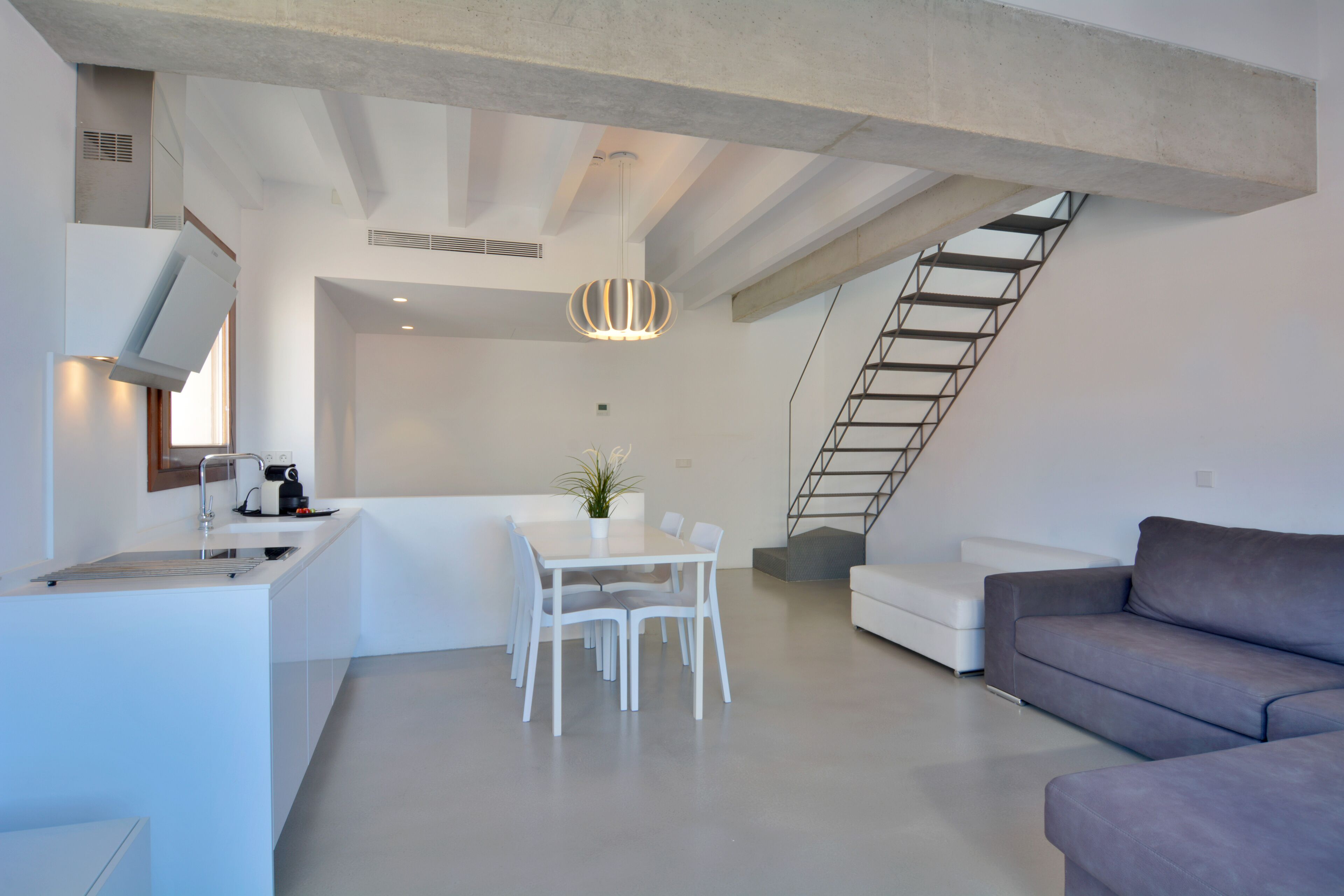 A modern kitchen with a dining area, a staircase, and a living room with a sofa.