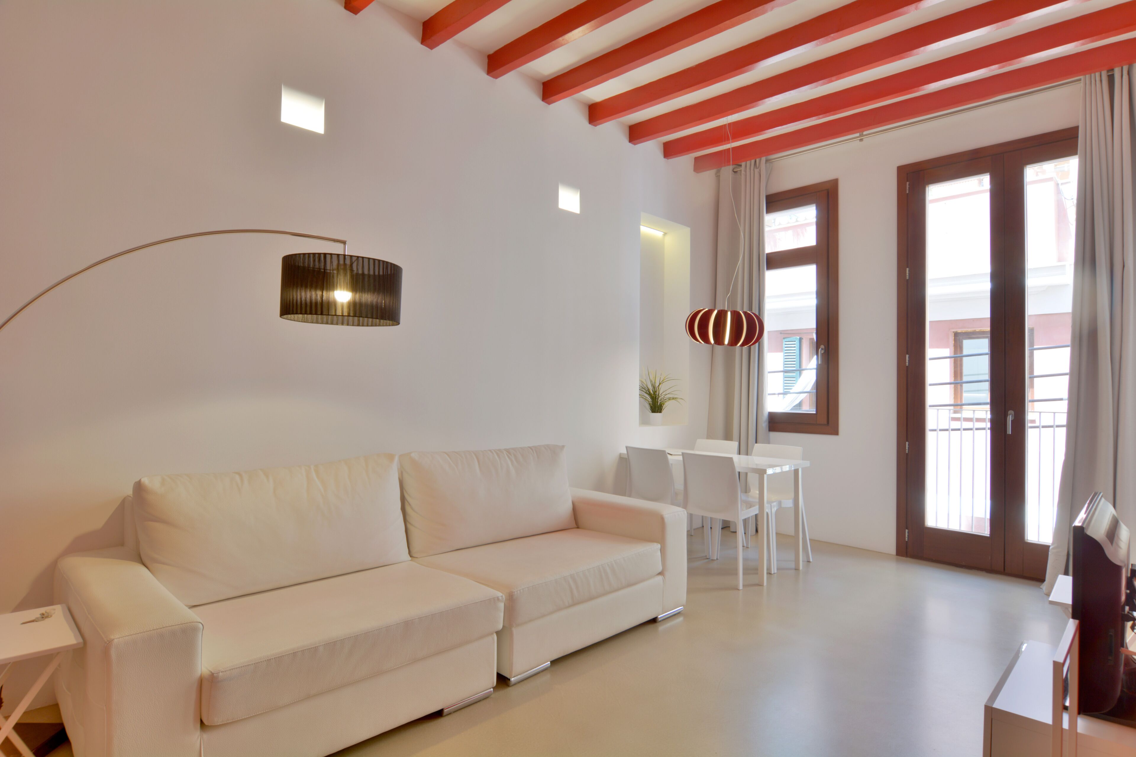 A modern living room with a white sofa, a dining table with chairs, a floor lamp, and a large window with curtains.