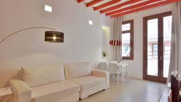 A modern living room with a white sofa, a dining table with chairs, a floor lamp, and a large window with curtains.