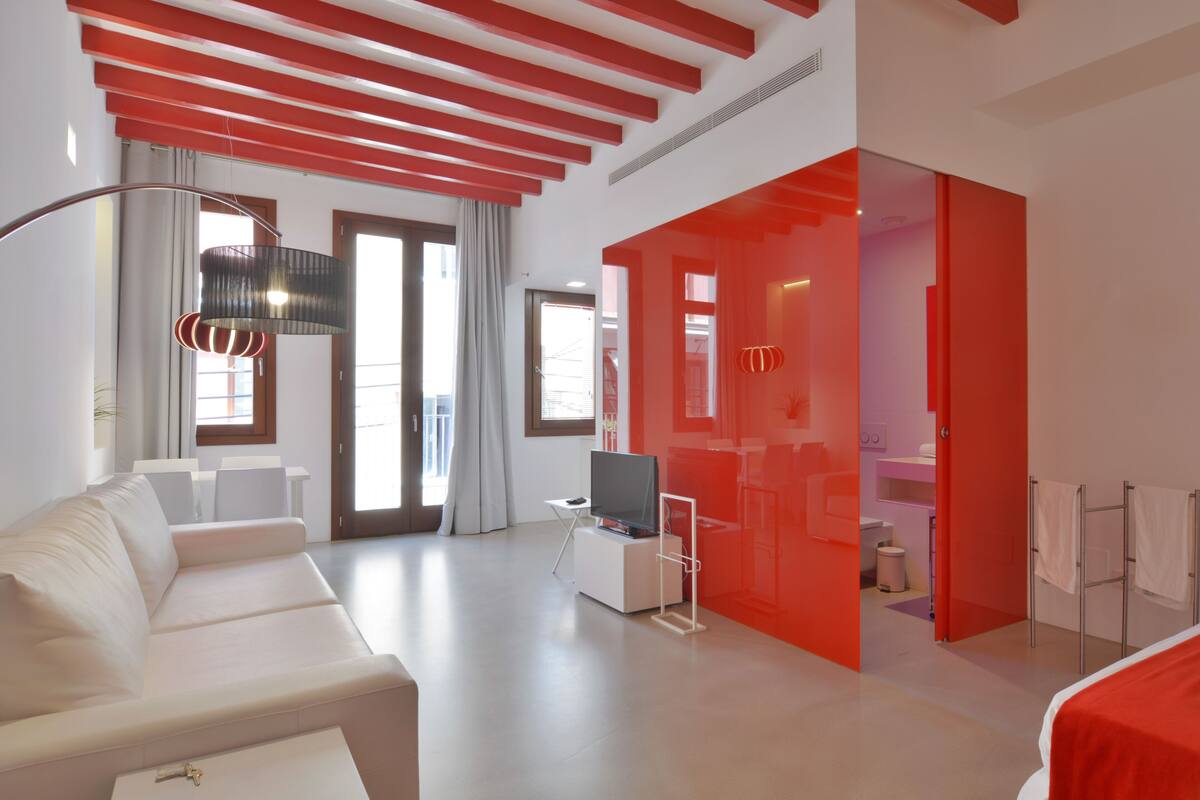 Een moderne hotelkamer met een witte bank, een televisie op een witte standaard, en een rode accentmuur.