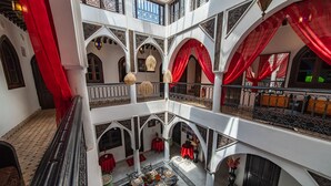 A multi-level interior with a central courtyard, red drapes, and a dining area with tables set for guests. - Riad Balkisse (Marrakech)