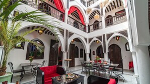 A spacious courtyard with a dining area, red cushioned seating, and a decorative table. - Riad Balkisse (Marrakech)