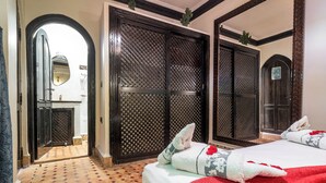 Une chambre d’hôtel avec un sol carrelé, un lit avec une literie blanche et rouge, un miroir et une armoire à motifs en treillis.