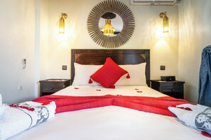 A hotel room with a large bed, two bedside tables, a wall-mounted mirror, and two wall sconces. - Riad Balkisse (Marrakech)