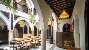 Une cour spacieuse avec une table et des chaises en bois, entourée d’arches et de colonnes, et une enseigne indiquant le nom du lieu.