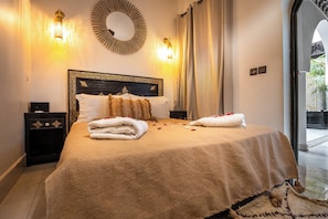 A neatly made bed with towels and rose petals, a decorative mirror, and wall sconces.