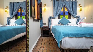 Une chambre avec deux lits, chacun recouvert d’une courtepointe bleue assortie à des coussins, une petite table de chevet en bois et un miroir fixé au mur.