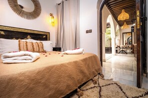 Une chambre élégamment aménagée, dotée d’un grand lit, d’un miroir décoratif et offrant une vue sur un espace extérieur avec une table et des chaises.
