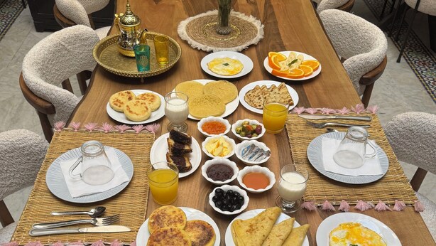Une table de petit-déjeuner dressée avec des assiettes de crêpes, d’omelettes et de viennoiseries, accompagnées de diverses sauces et boissons.