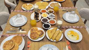 A breakfast table set with plates of pancakes, omelets, and pastries, accompanied by various condiments and beverages.