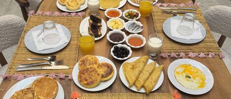 A breakfast table set with plates of pancakes, omelets, and pastries, accompanied by various condiments and beverages.
