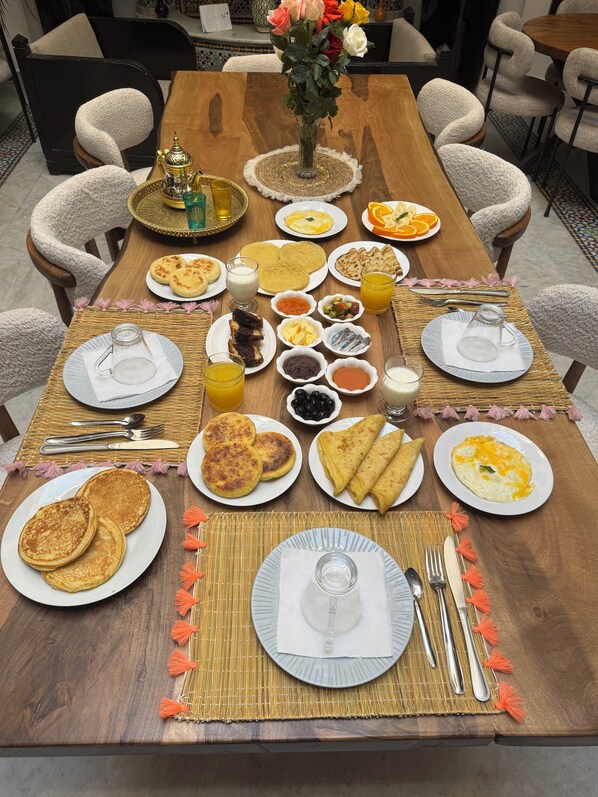 A breakfast table set with plates of pancakes, omelets, and pastries, accompanied by various condiments and beverages. - Riad Balkisse (Marrakech)