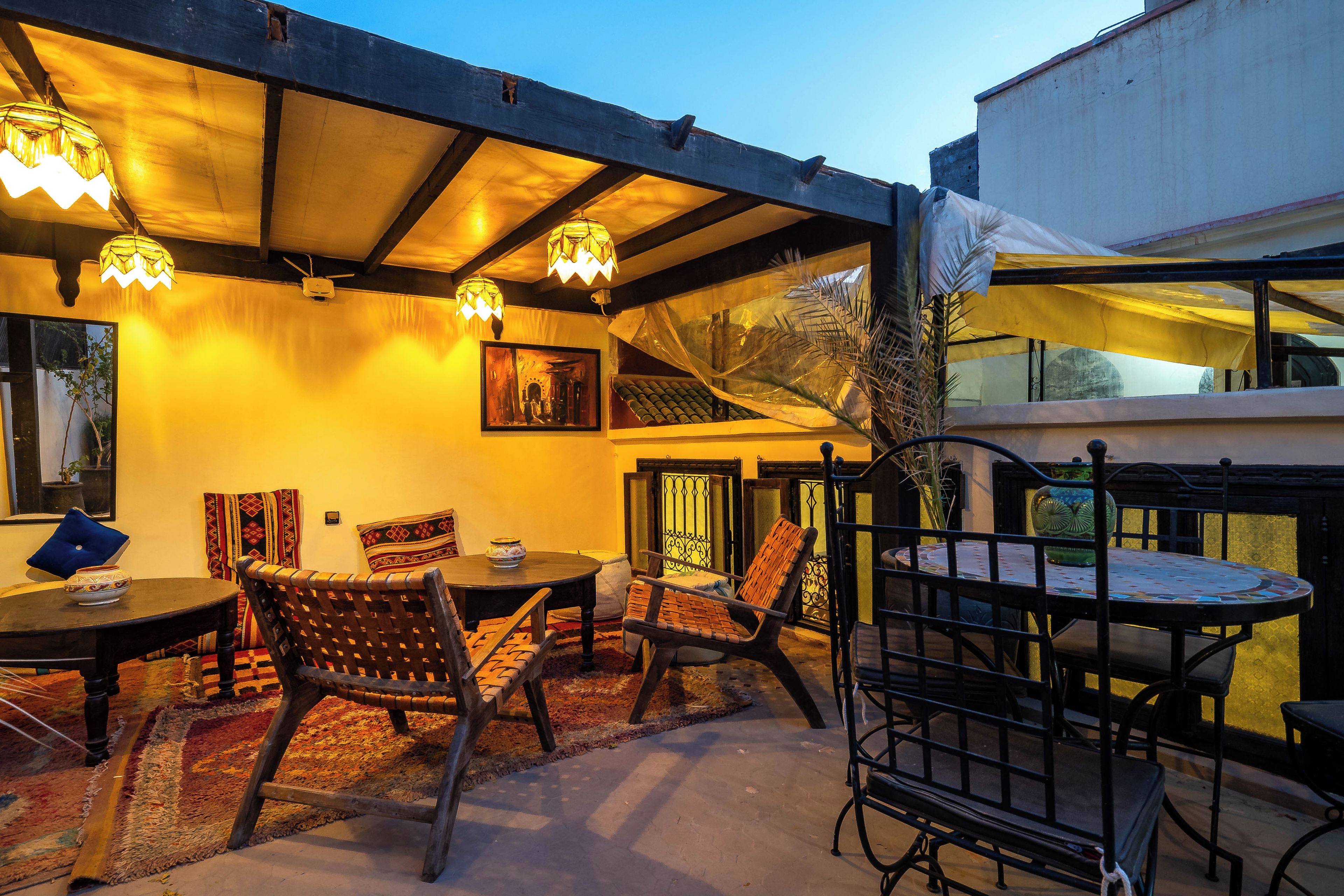 An outdoor seating area with tables and chairs, a decorative wall, and a ceiling with hanging lights.