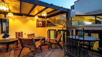 An outdoor seating area with tables and chairs, a decorative wall, and a ceiling with hanging lights.