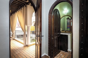 An interior corridor with a tiled floor, a wooden door, and a view of a balcony with a railing.