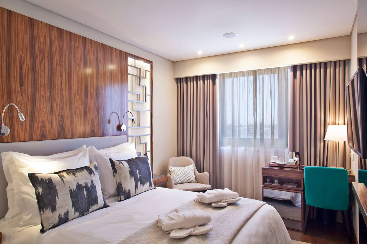 Une chambre d’hôtel avec un grand lit, un bureau, une chaise et une vue sur la ville par la fenêtre.