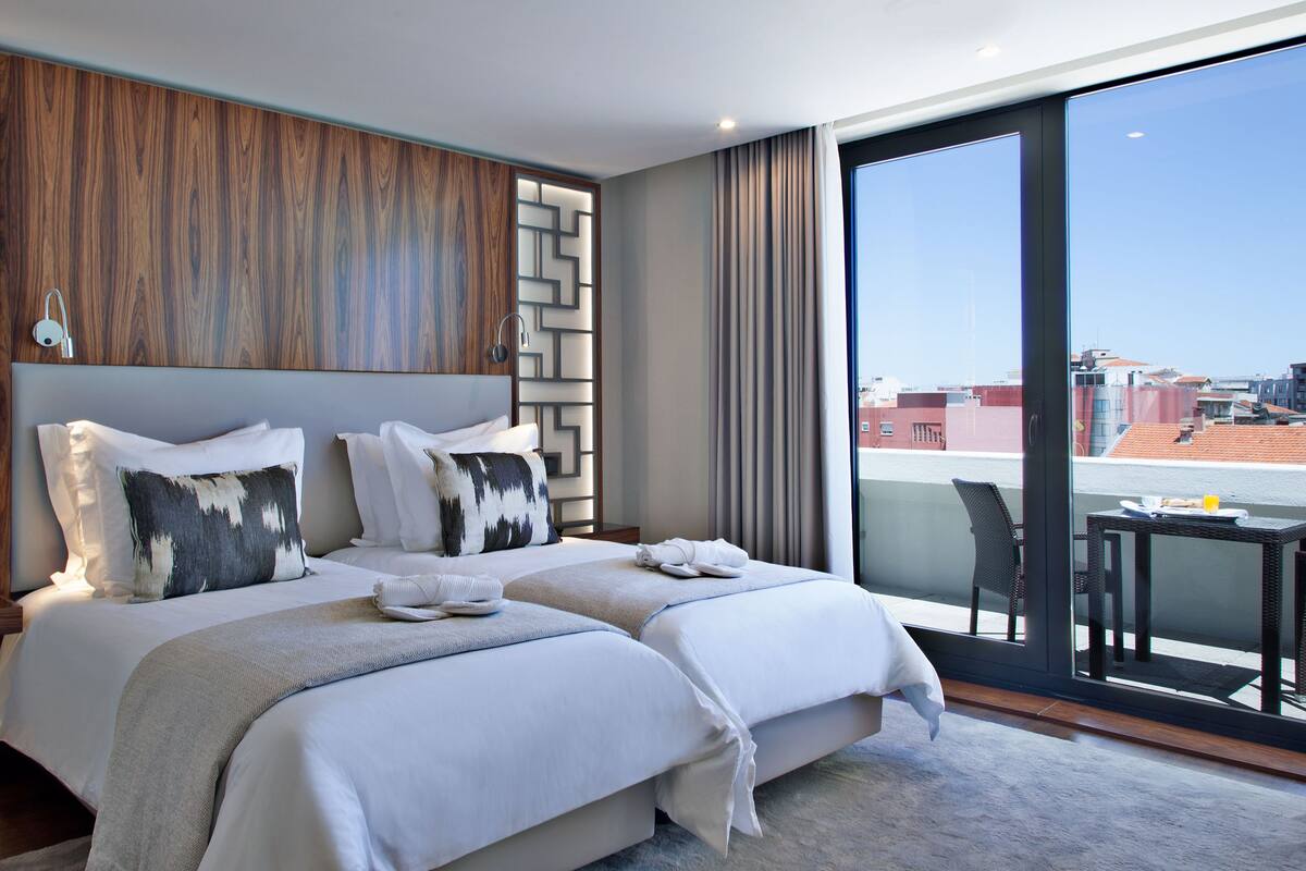 Une chambre d’hôtel moderne avec deux lits, une grande fenêtre et une vue sur le paysage urbain.