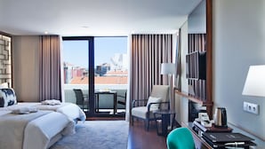 A hotel room with two beds, a desk, a chair, a TV, and a view of the city.