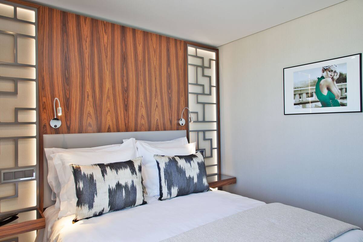 Une chambre d’hôtel moderne avec une tête de lit en bois, du linge de lit blanc et un tableau encadré au mur.