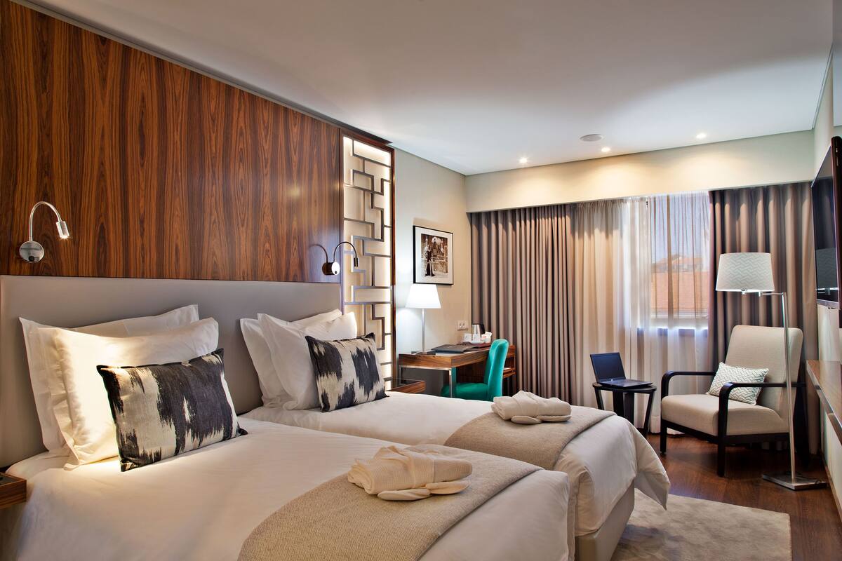 Une chambre d’hôtel avec deux lits, un bureau, une chaise, une télévision et une fenêtre avec des rideaux.