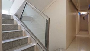 A modern interior with a staircase leading to a lower level, a glass railing, and a hallway with a ceiling light. - Hotel Executive Residency (Pune)