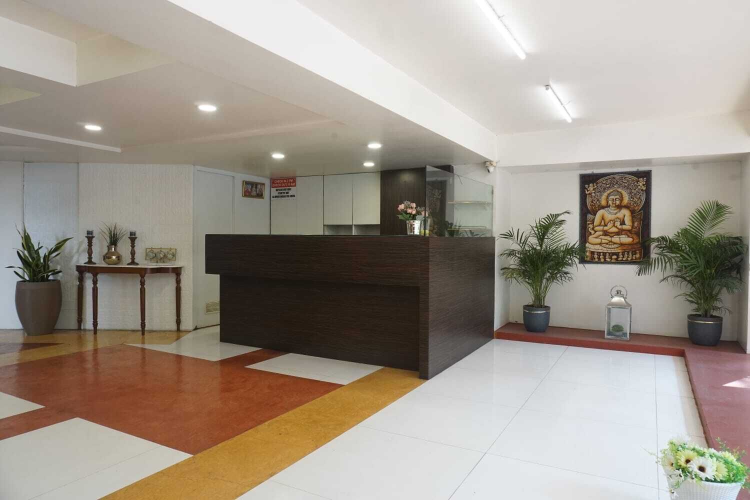 A reception area with a dark wooden desk, potted plants, and a Buddha statue on the wall.