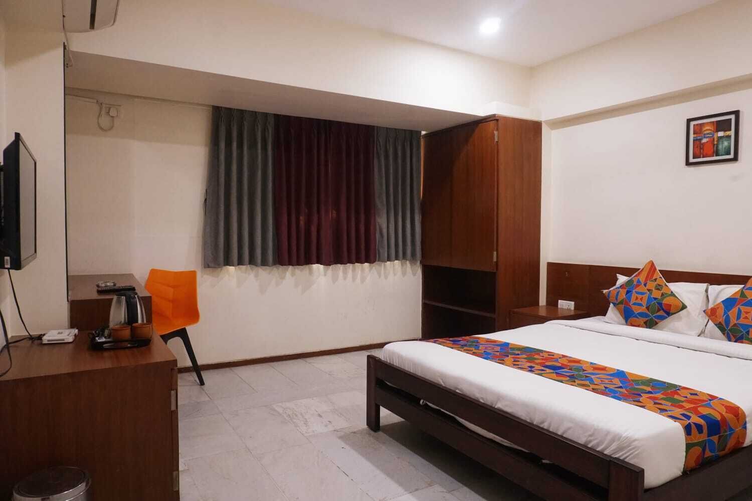 A hotel room with a bed, a desk with a chair, a TV, and a window with curtains.