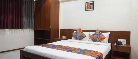 A hotel room with a bed, a wooden wardrobe, a nightstand, a telephone, and a painting on the wall.