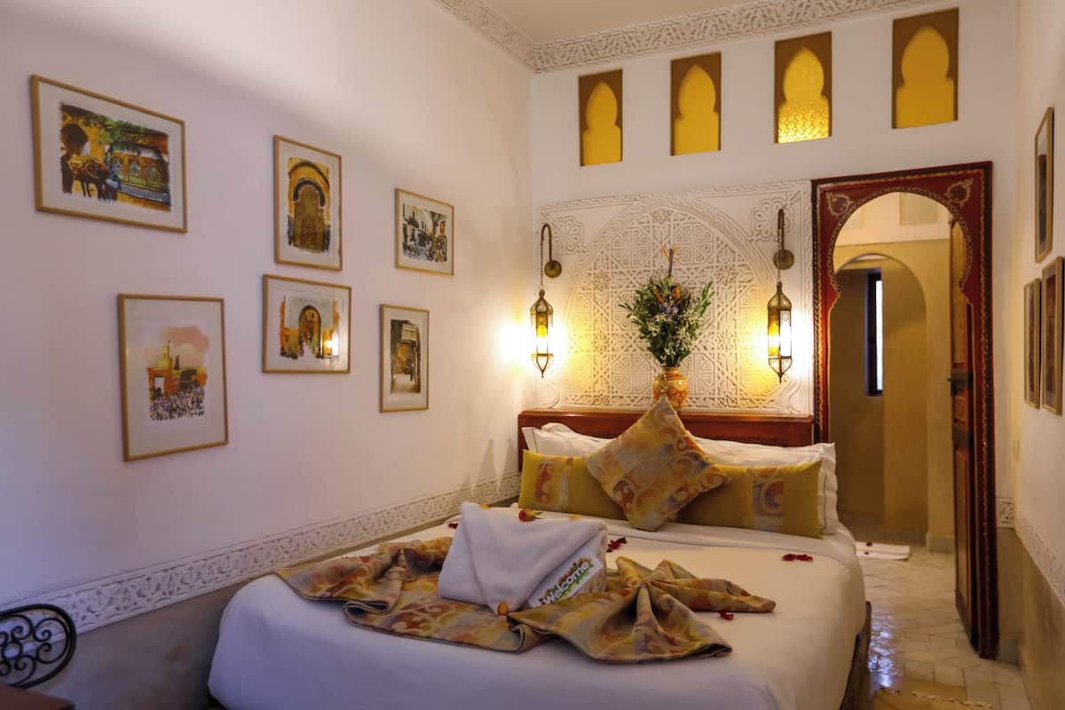 Habitación de hotel con cama, decoración mural, mesita de noche y espejo decorativo.