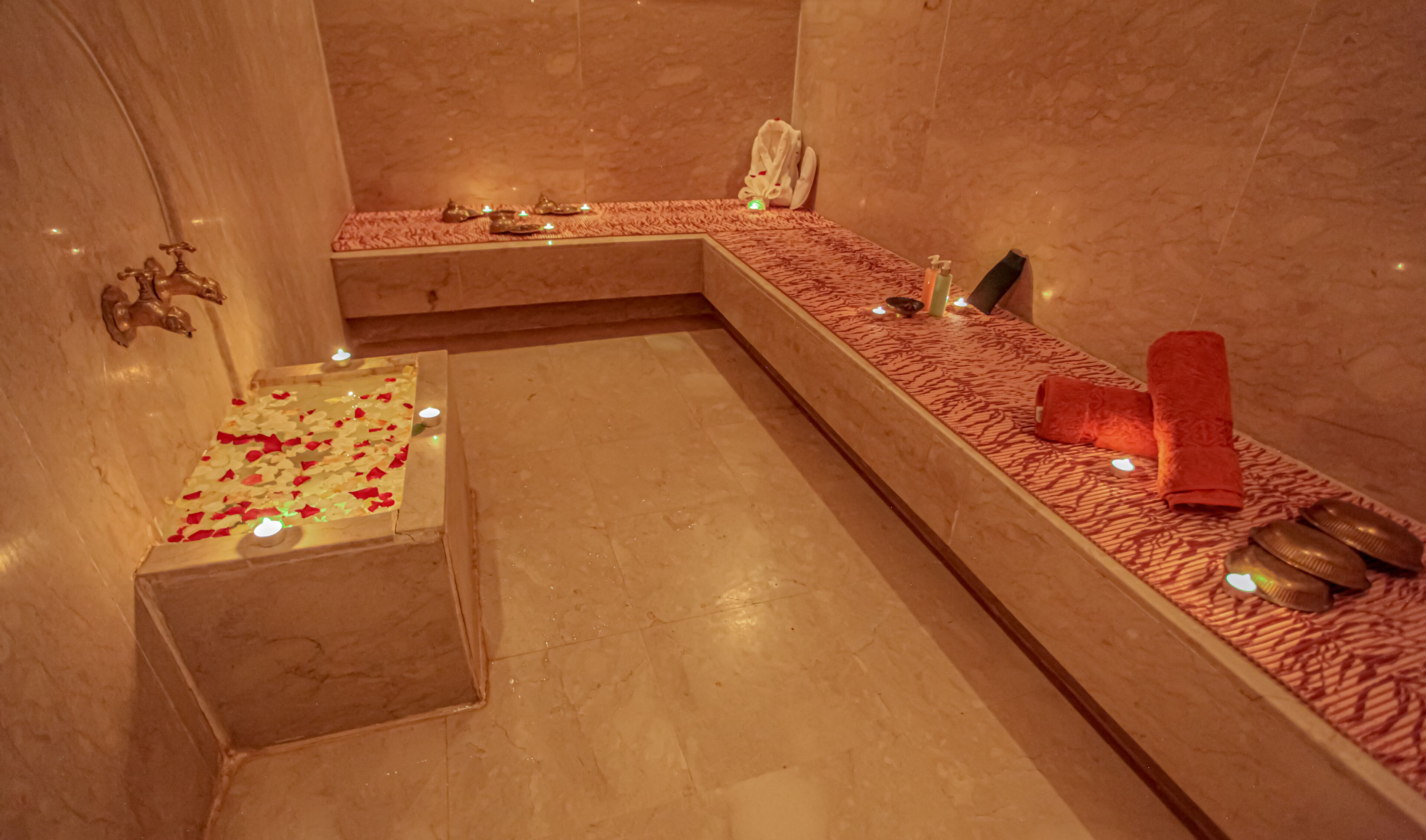 A spa area with a bathtub, a small pool with rose petals, candles, and towels.