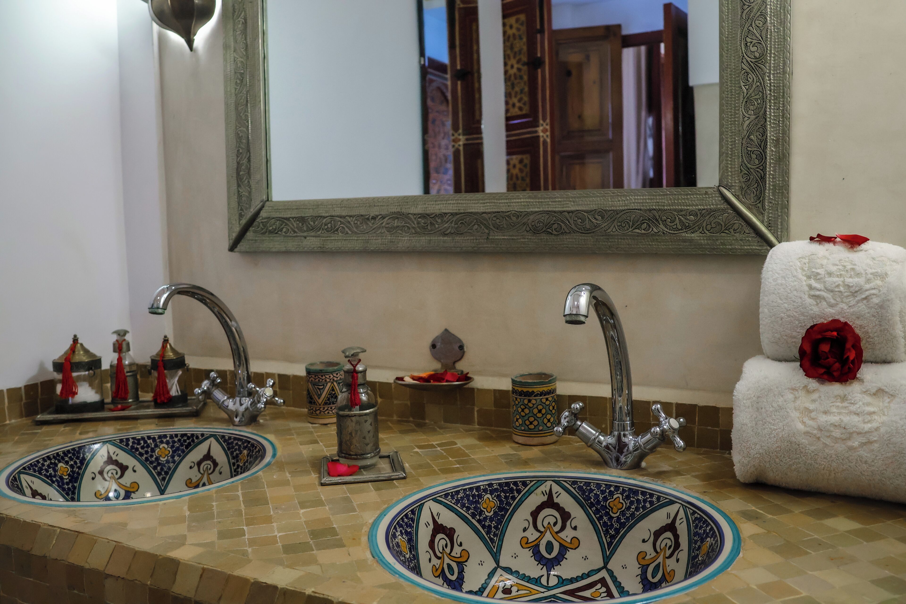 Un baño con dos lavamanos, cada uno con un lavabo de azulejos decorativos, un espejo con un marco ornamentado y un perchero con una rosa roja.