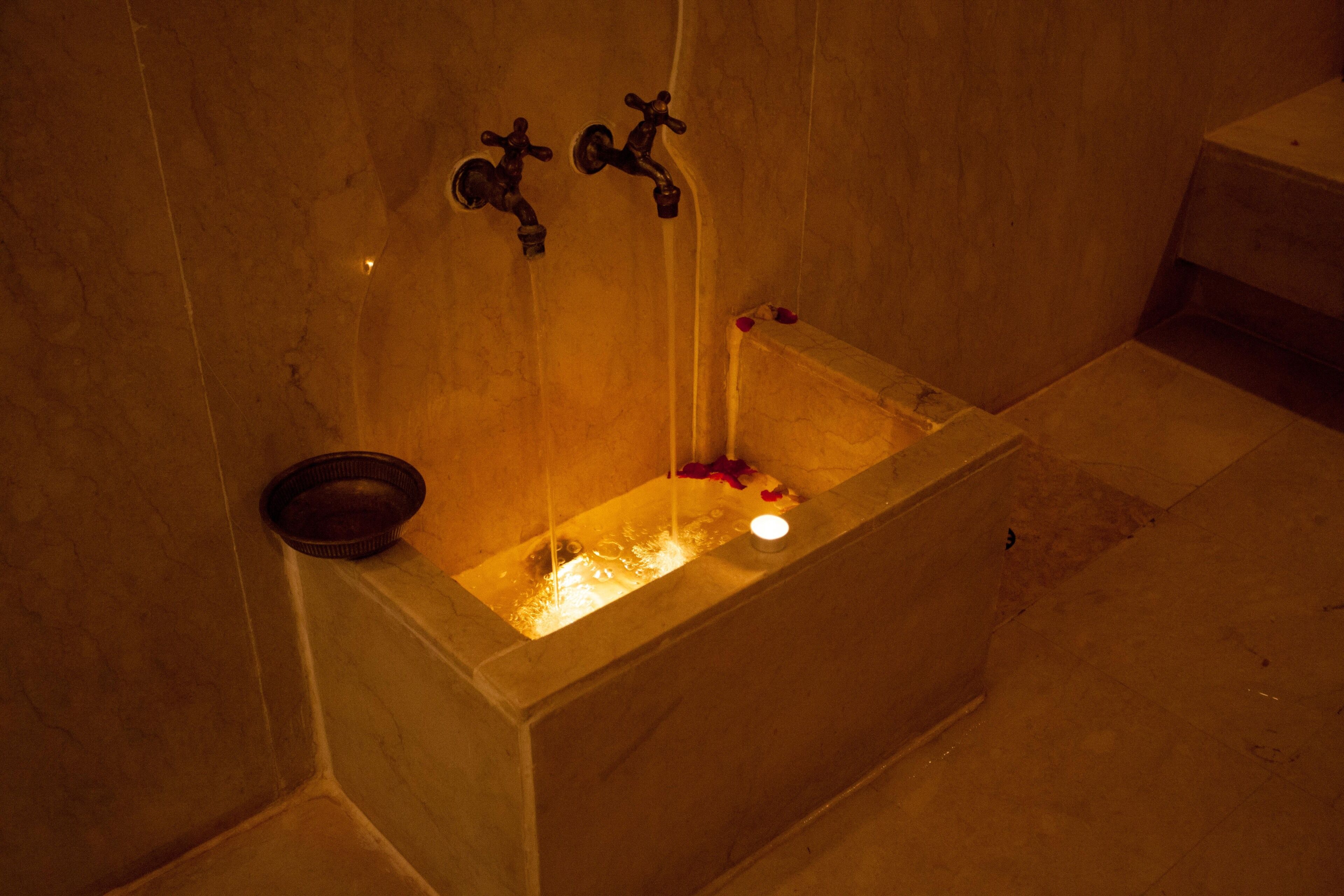 A bathtub with running water, a candle, and rose petals.