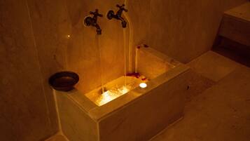 A bathtub with running water, a candle, and rose petals.