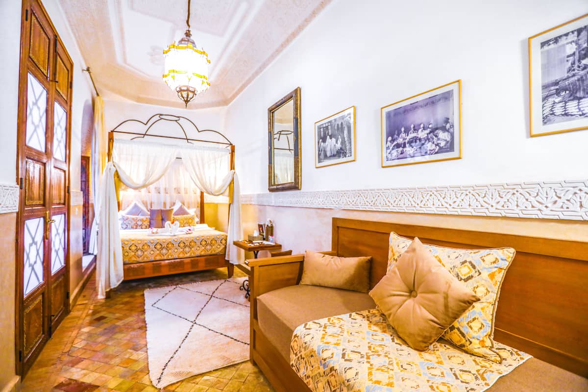 Una habitación con una cama, una mesita de noche y un espejo. Hay cuadros enmarcados en la pared.