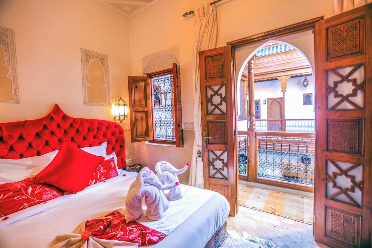 Habitación de hotel con un cabecero tapizado rojo, una cama con ropa blanca y vista a un patio a través de una puerta abierta.