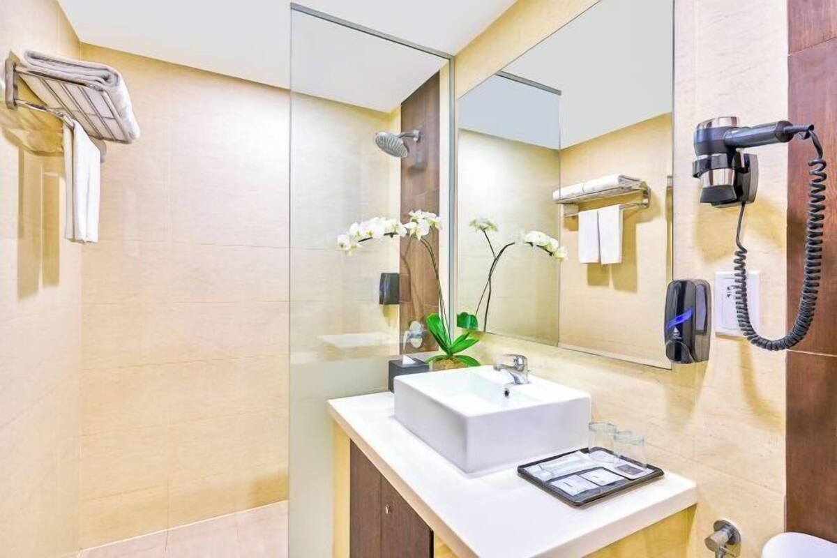 A modern bathroom with a white sink, a glass shower enclosure, a handheld hair dryer, and a mirror.