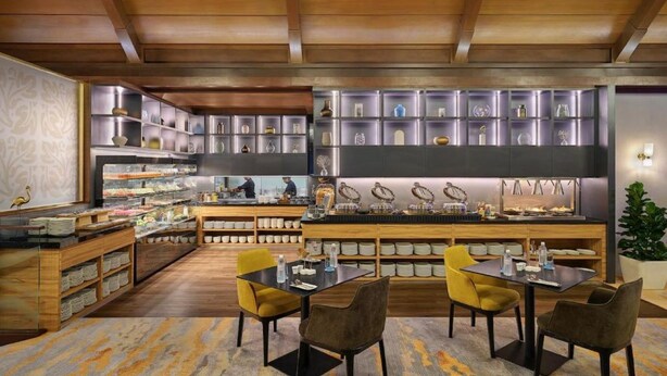 Un interior moderno con vigas de madera en el techo, una zona de bar central con asientos y estantes con diversos objetos.