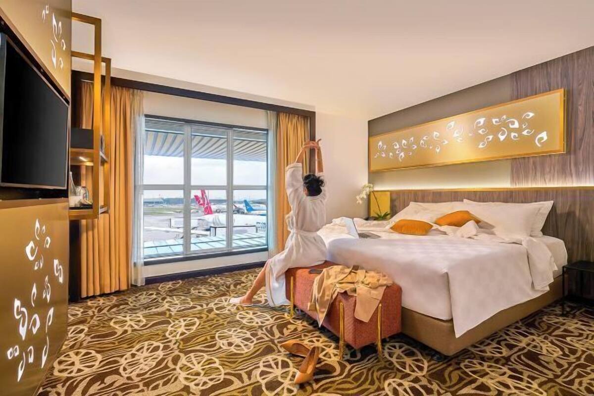 A hotel room with a bed, a TV, a large window, and a view of the outside.