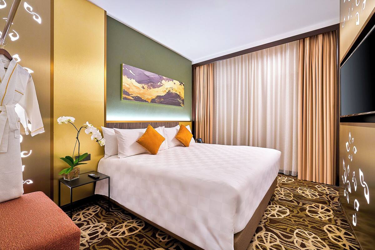 A hotel room with a bed, a nightstand, a TV, a painting on the wall, and a patterned carpet.