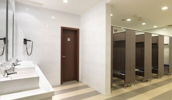 Un baño moderno con paredes de mármol blanco, una puerta de madera y una hilera de cabinas de madera.