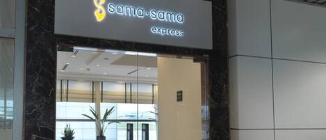 A hotel entrance with a sign reading "sama.sama express" and a directional sign pointing to the hotel.