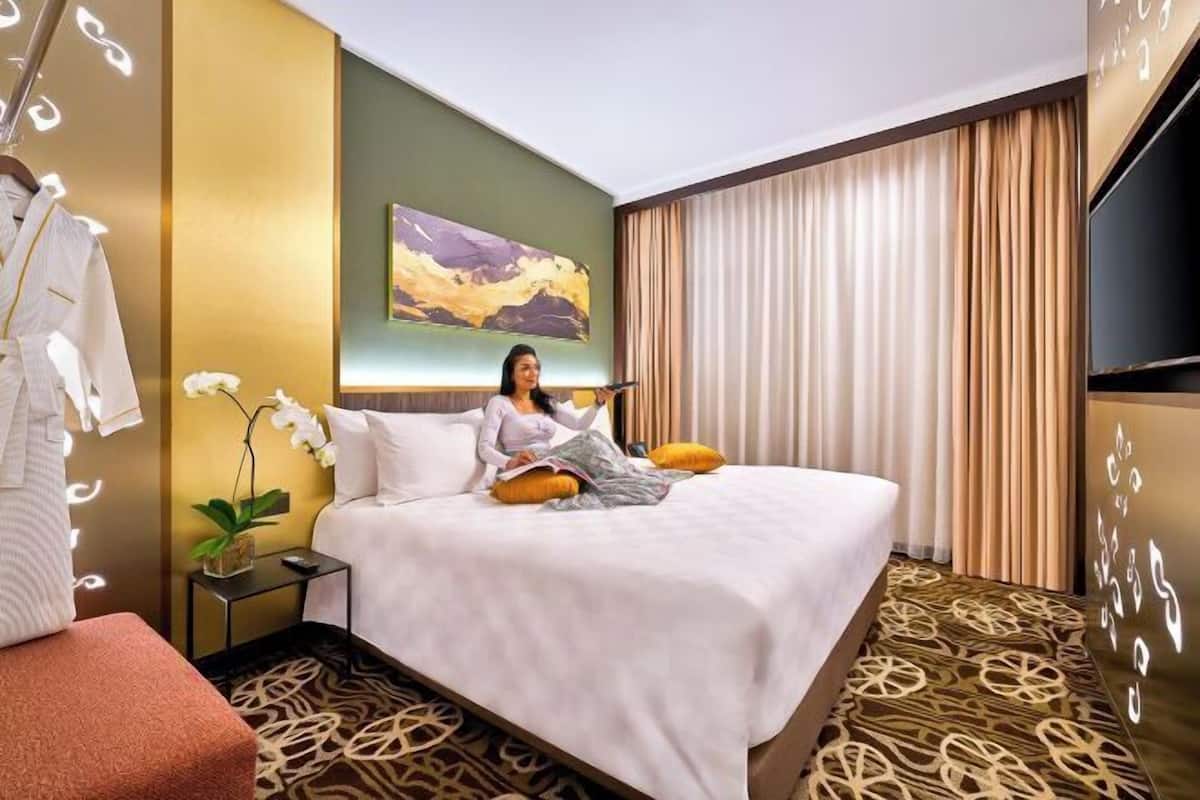 A hotel room with a bed, a nightstand, a TV, a painting on the wall, and a window with curtains.