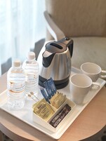 Una bandeja con botellas de agua, una cafetera, sobres de azúcar y tazas de café sobre una mesa.
